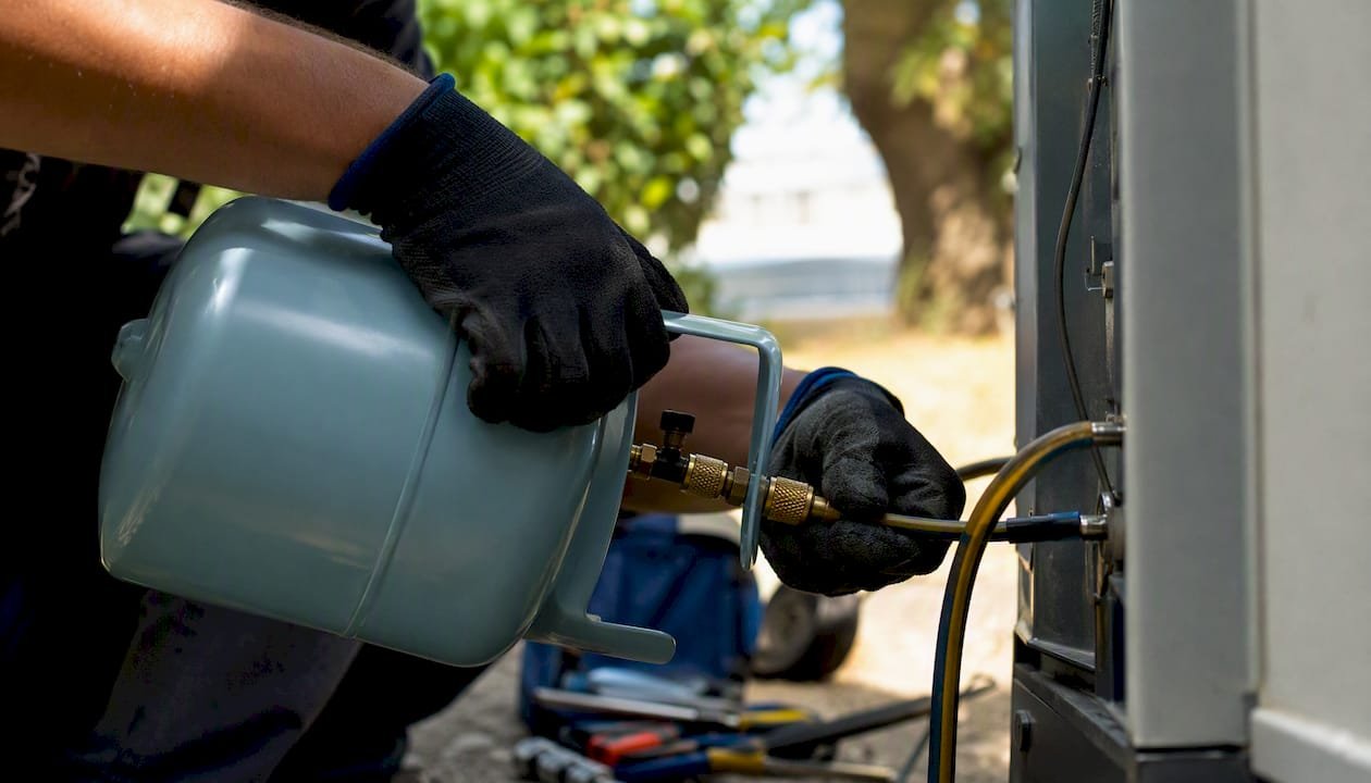 Hands pouring refrigerant into HVAC system